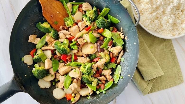 Chicken, vegetable, and almond stir fry in wok with wooden spatula