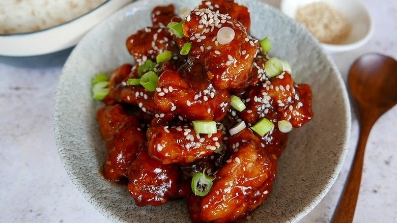 Homemade General Tso's chicken in bowl, garnished with sesame seeds and chopped green onions