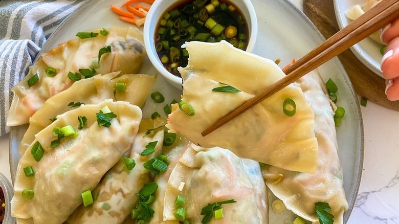 Potstickers on plate with soy-scallion dip, with one dumpling being lifted with chopsticks