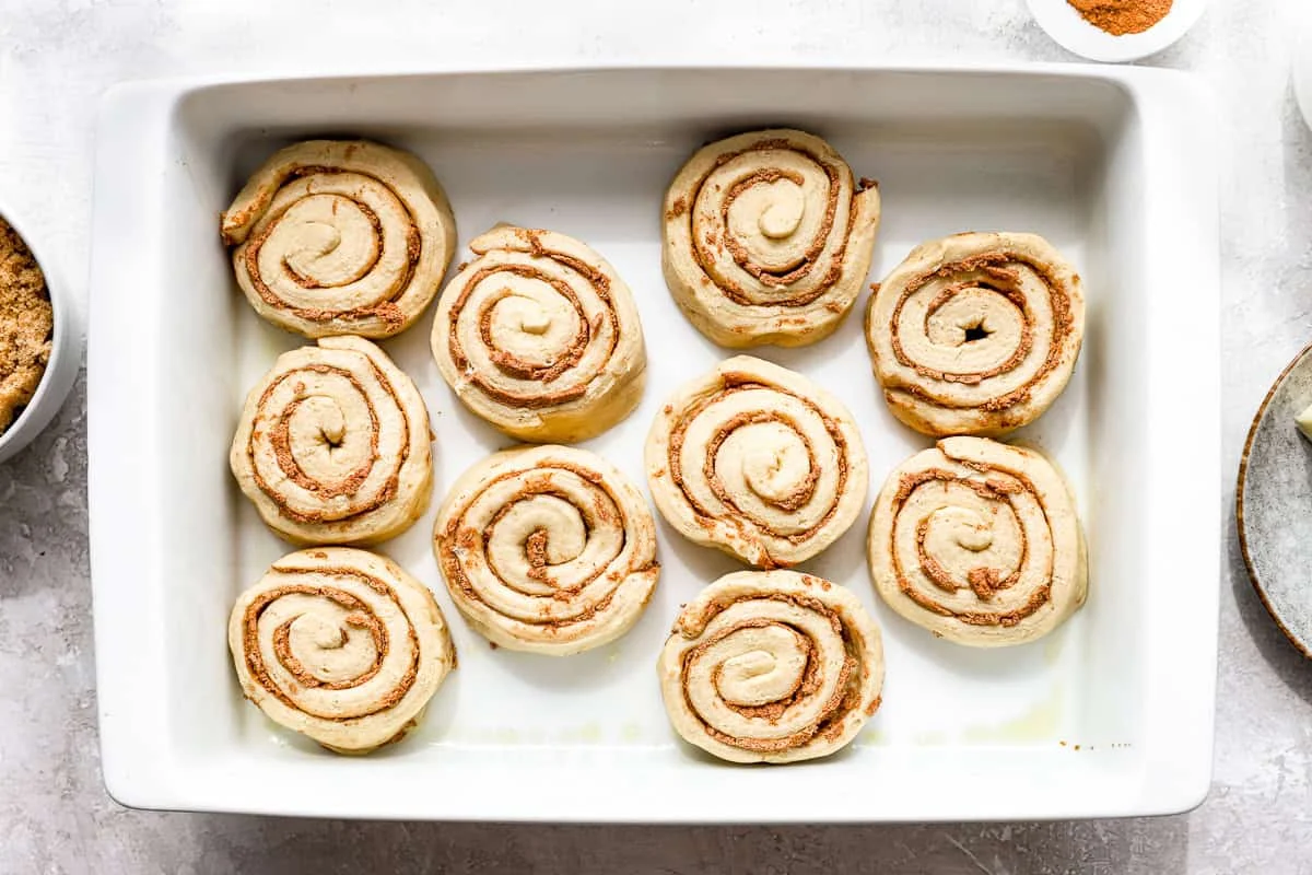 Gooey heavy cream cinnamon rolls topped with icing in a baking dish with caramel sauce underneath.