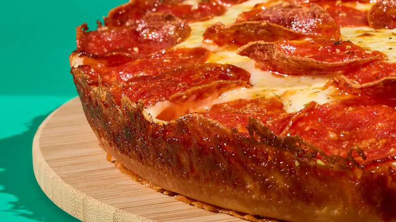 The edge of a pepperoni pan pizza with a crispy crust sitting on a wooden board