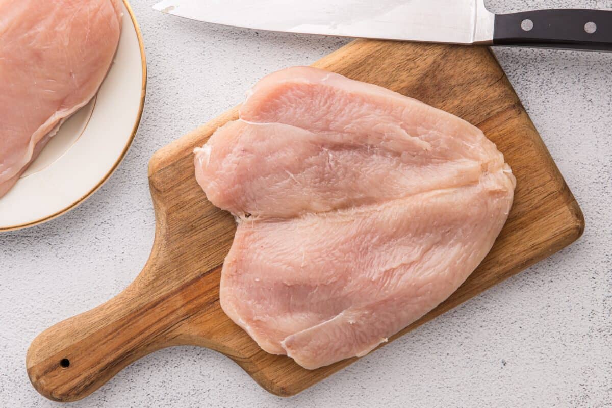 Raw butterflied chicken breast on a wooden cutting board with a knife