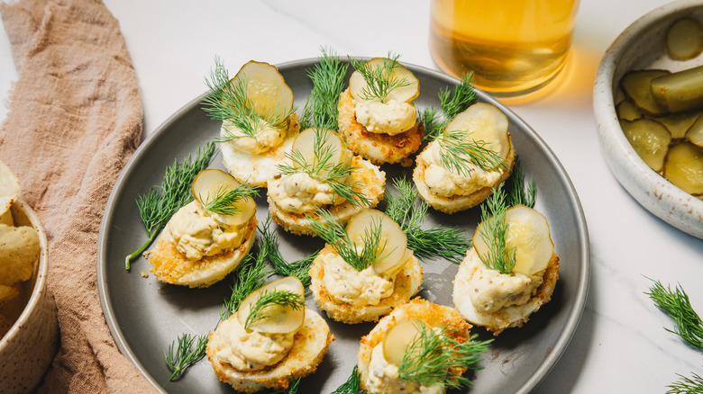 Pickle and dill topped deviled eggs on a grey plate.
