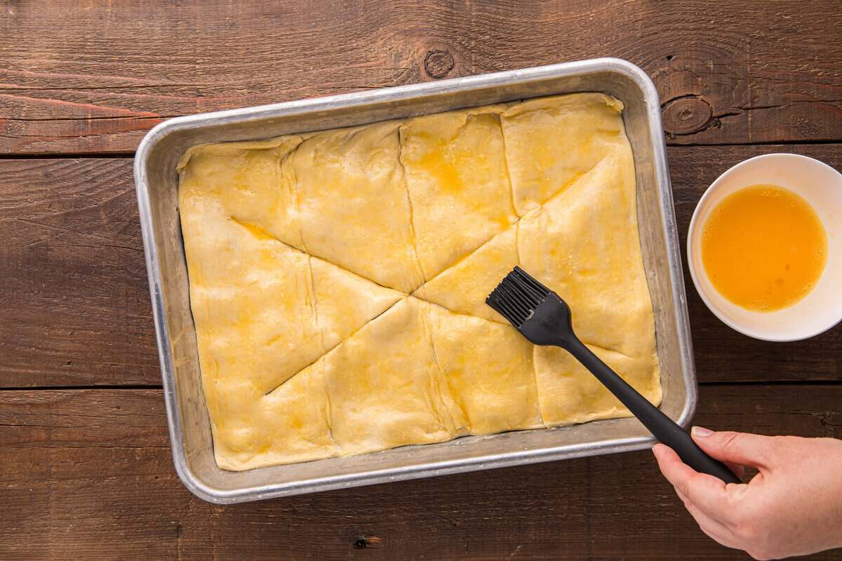 Egg wash being brushed over the puff pastry topping with a silicone brush before baking