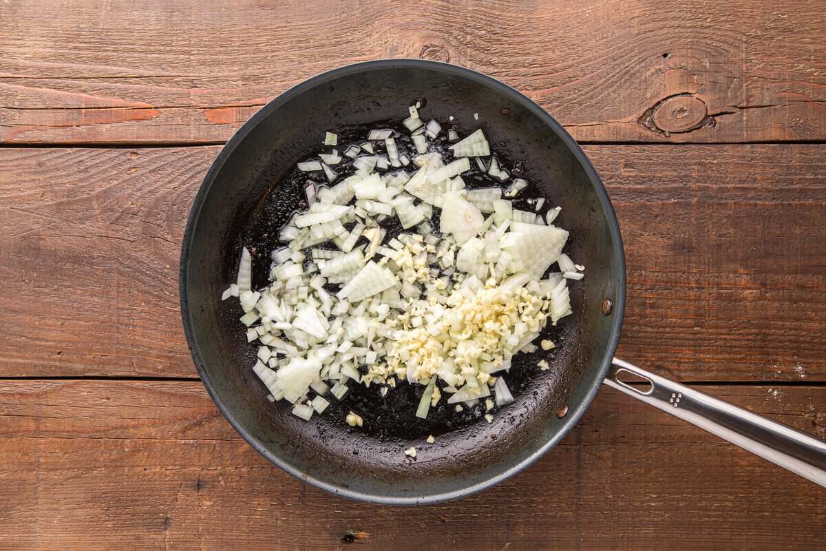 Diced onion and minced garlic cooking in a dark skillet in beef drippings