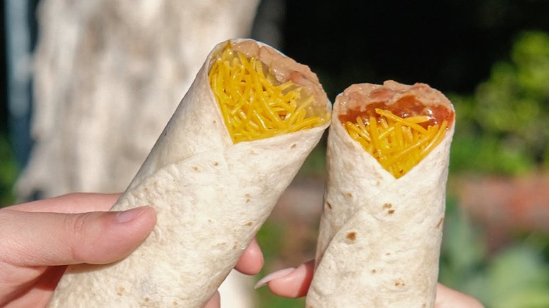 Two handheld Del Taco value bean and cheese burritos