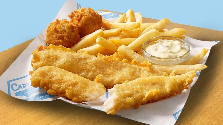 A two-piece fish meal from Captain D's with two pieces of fish, two hushpuppies, fries, and a ramekin of tartar sauce on a black background