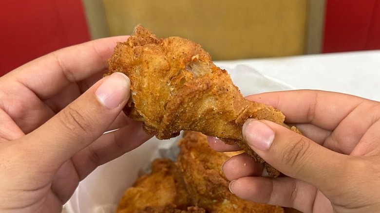 Hands holding a drumstick from Kentucky Fried Chicken bucket