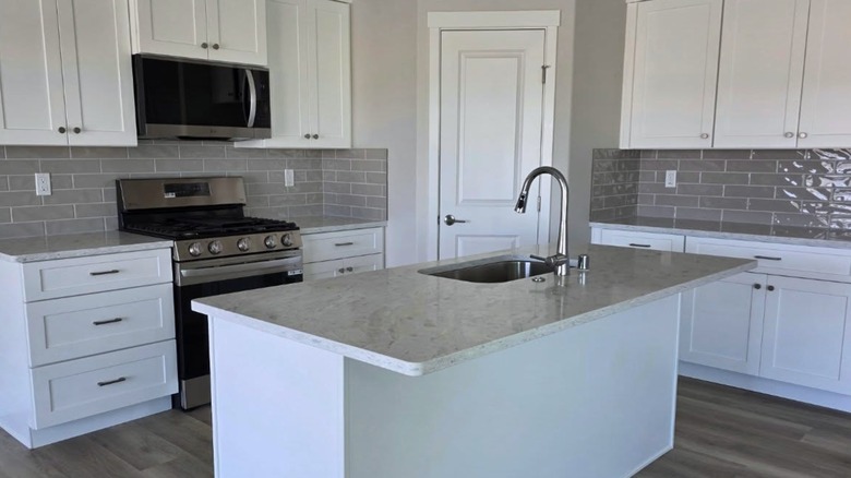 Kitchen with gray counters, gray tile backsplash, white cabinets, and steel oven