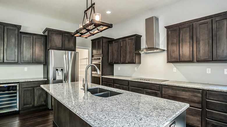 Kitchen with dark wood cabinets, speckled black and white gray counters, and stainless steel appliances and hardware