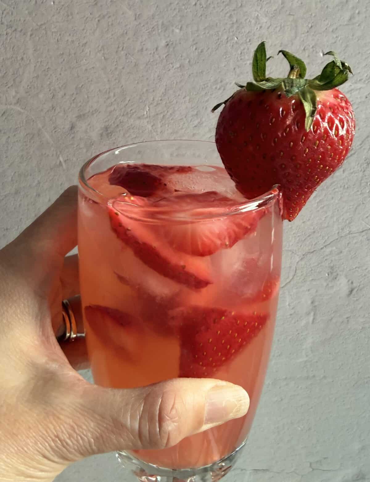 Hand holding a glass of Red Robin strawberry lemonade with strawberry slices in the drink and a whole strawberry on the rim