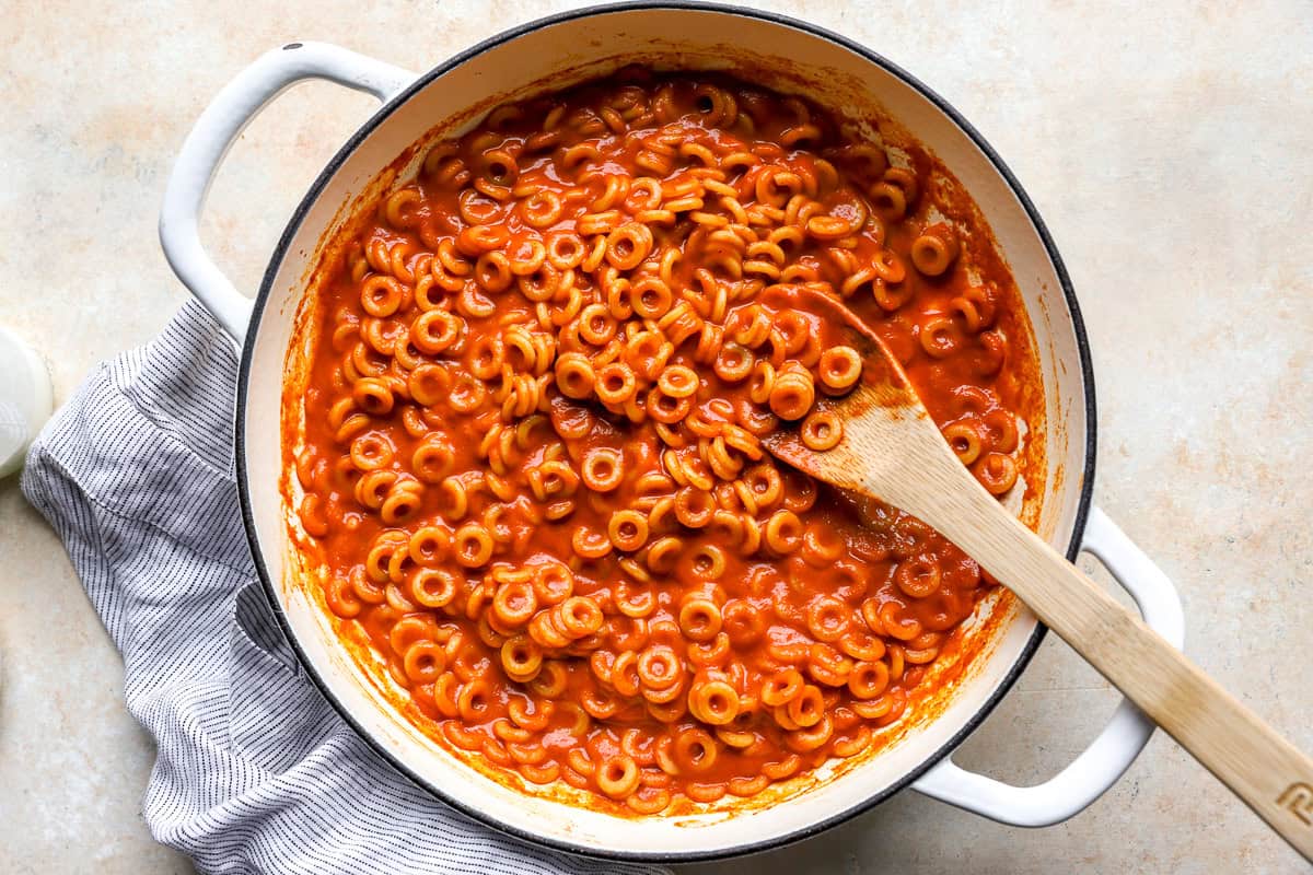 Anellini pasta fully coated in tangy tomato sauce in a large pot, before the cream is added.