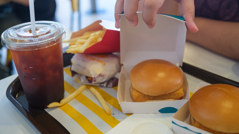 Hand holding open a Filet-O-Fish box on a tray full of McDonald's food and drinks