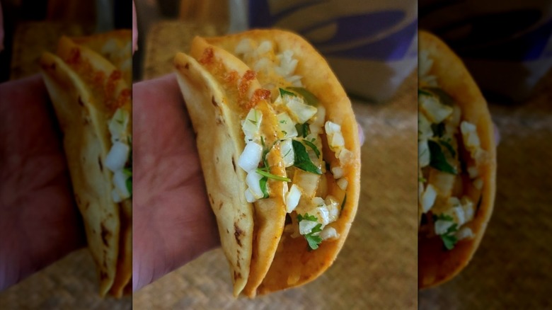 A Taco Bell steak fajita street chalupa held in someone's hand, topped with onion and cilantro