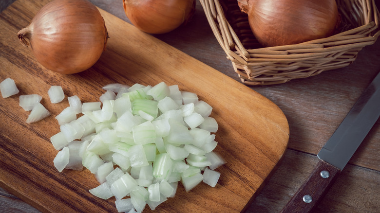 Sliced onions on a kitchen board next to a knife