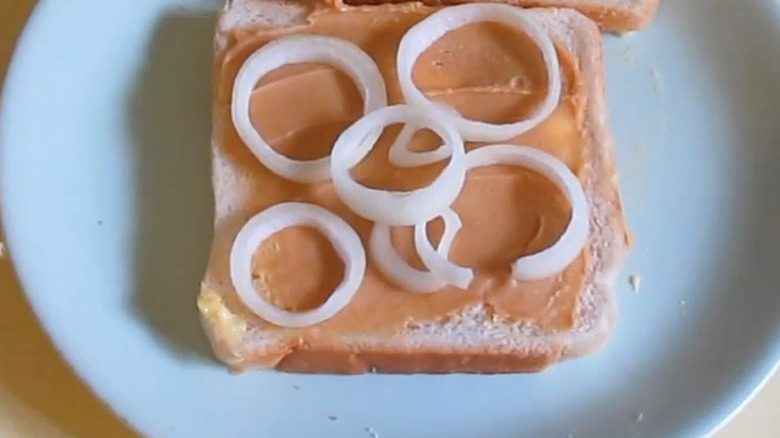 An open-faced peanut butter and onion sandwich on a white plate