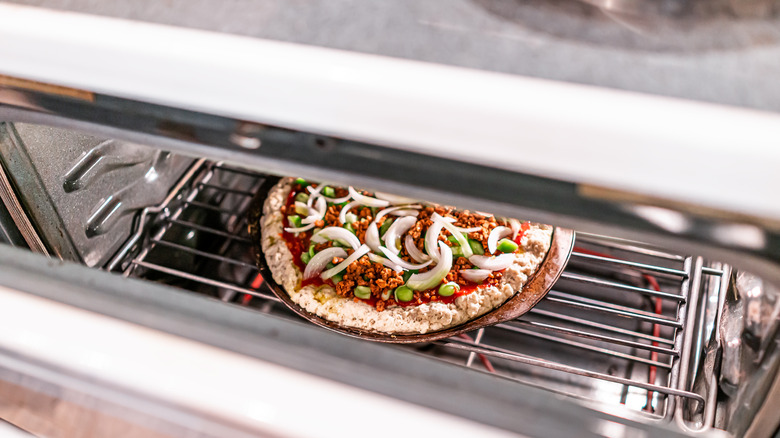 An oven door slightly cracked showing a frozen pizza topped with onion