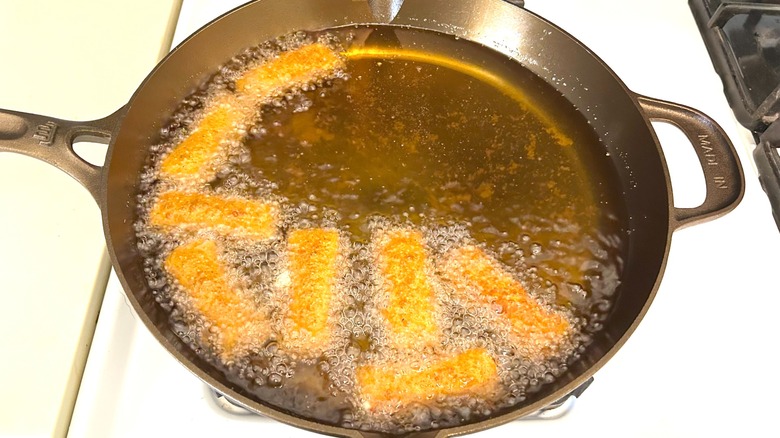 Mozzarella sticks frying in oil in Made In seasoned cast iron 12