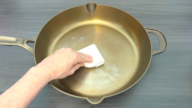 Hand spreading cooking oil onto the bottom of Made In seasoned cast iron 12