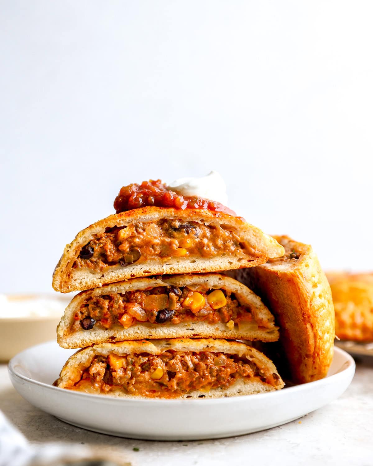 Loaded Taco Hot Pockets sliced in half and stacked on a white plate, topped with salsa and sour cream.