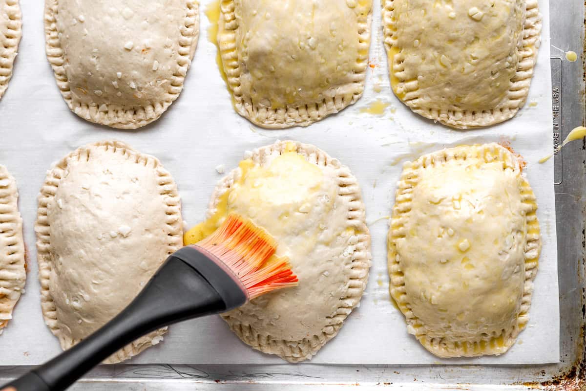 Egg wash being brushed onto the tops of unbaked taco hot pockets before baking.