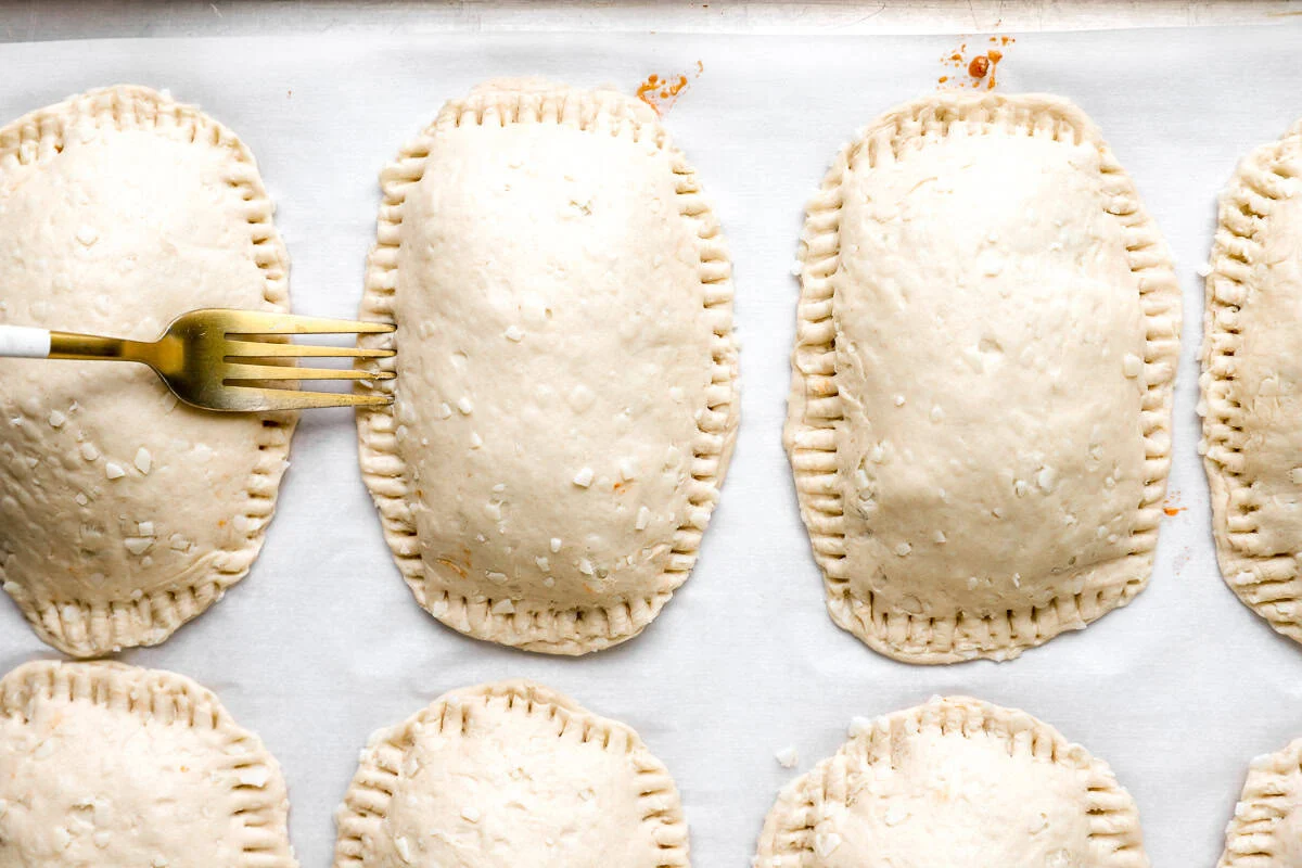 Unbaked taco hot pockets with the edges crimped shut using a fork on a parchment-lined sheet pan.
