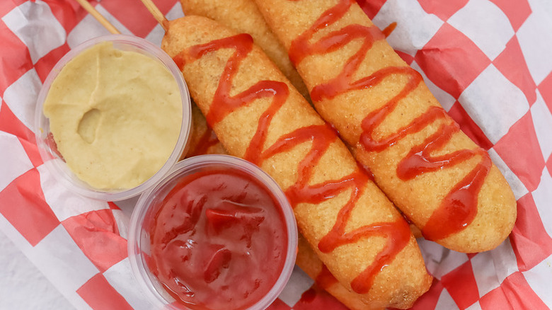 Corn dogs on red and white chequered paper with two pots of dip