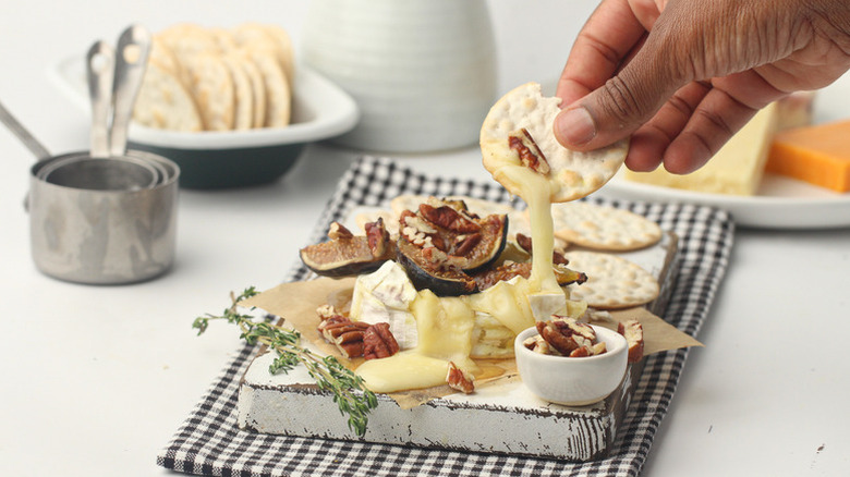 Hand dipping cracker into melty fig baked brie