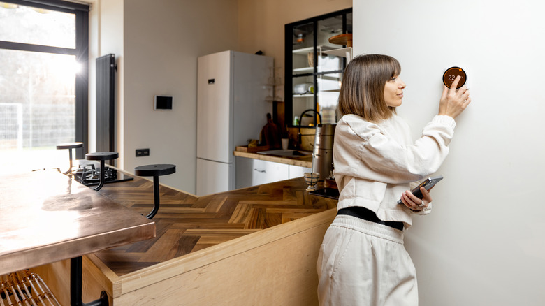 Woman adjusting thermostat on kitchen wall