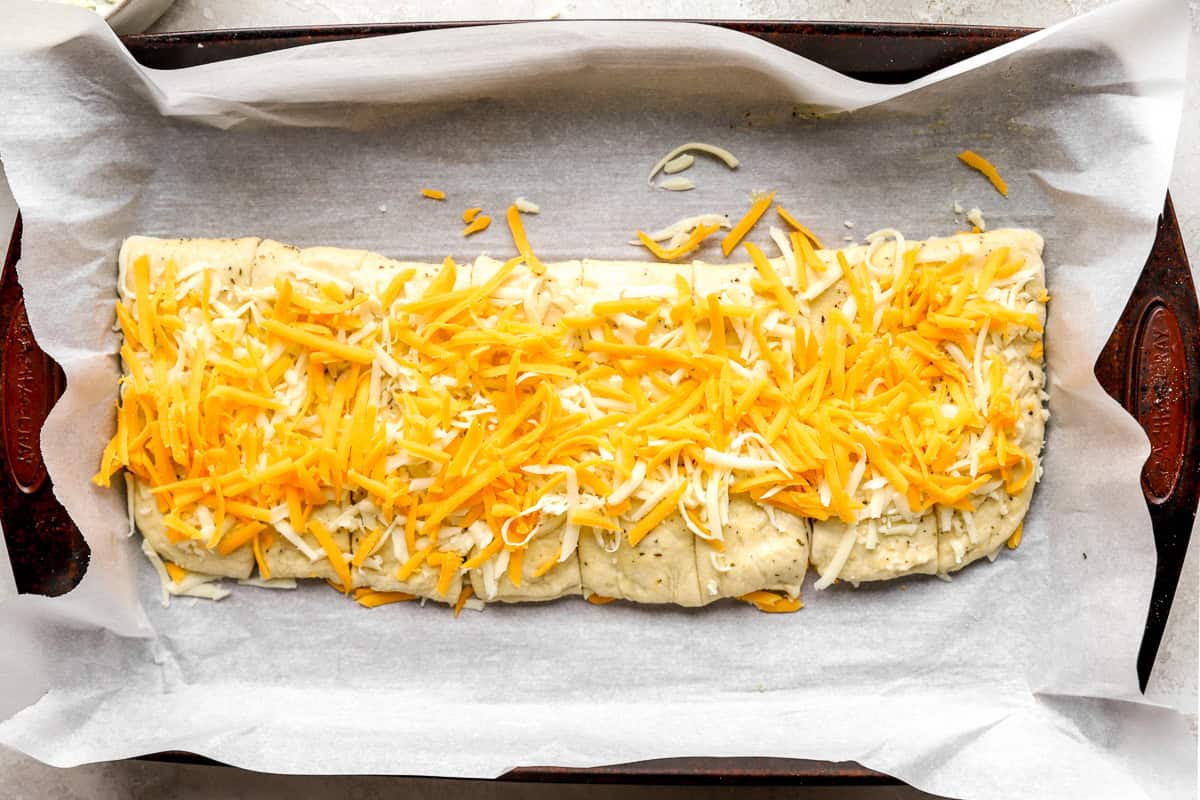 Unbaked stuffed cheesy bread topped with shredded mozzarella and cheddar cheese on a parchment-lined baking sheet