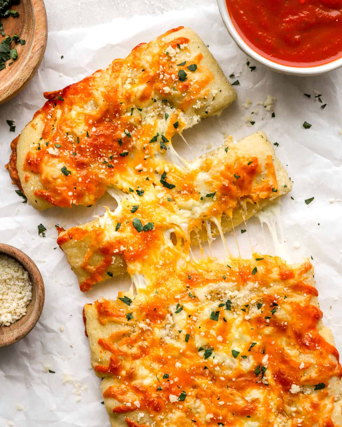 Overhead shot of sliced stuffed cheesy bread with melted cheese pulling apart, next to a bowl of marinara sauce