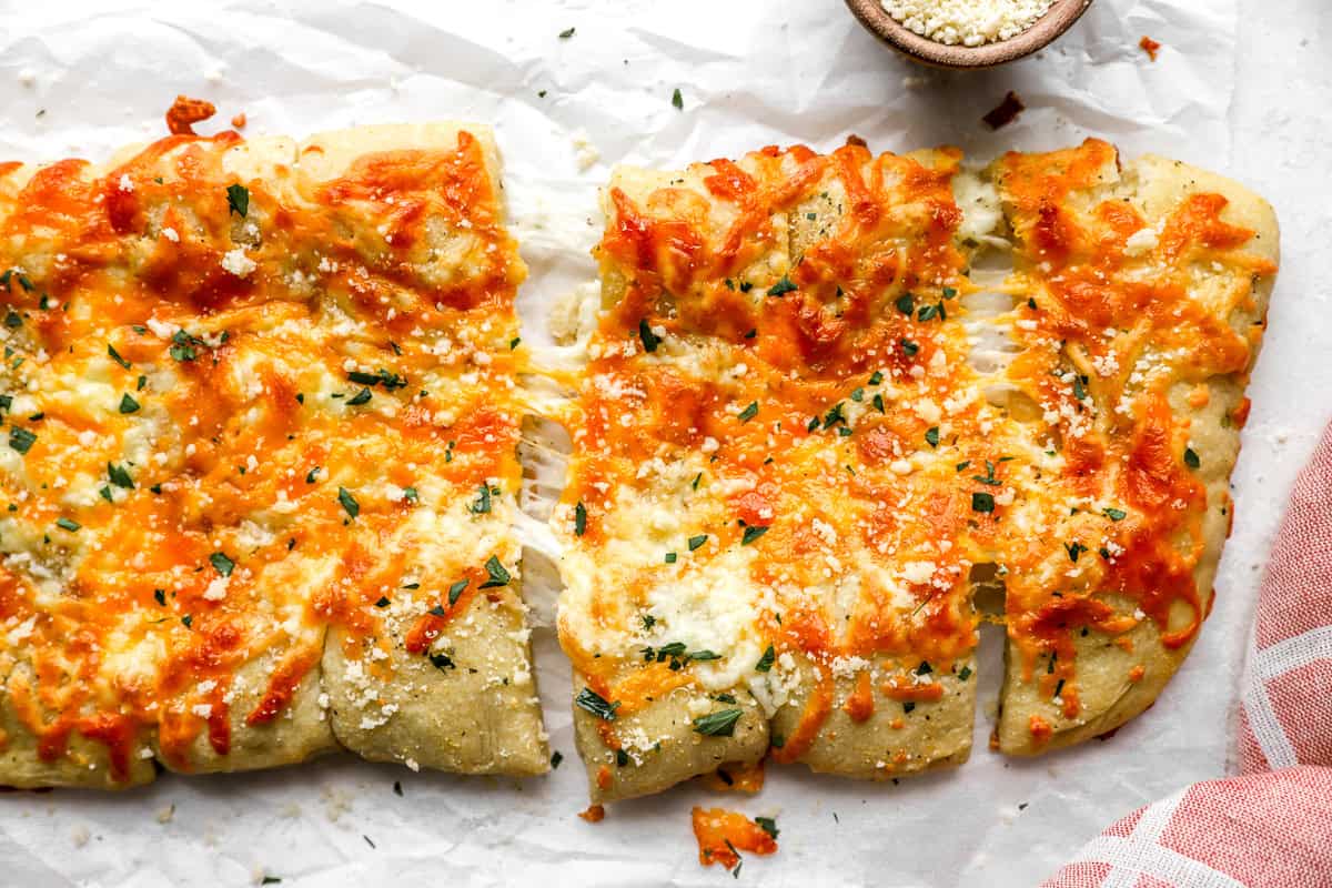 Overhead view of baked stuffed cheesy bread sliced into pieces with gooey cheese stretching between them
