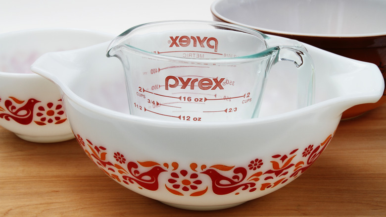 A glass Pyrex measuring cup featuring the Pyrex name in red over listed measurements sitting inside of a glass baking dish