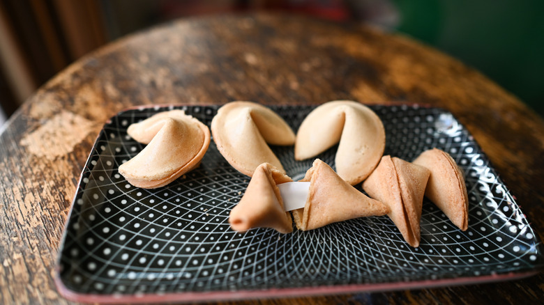 Fortune cookies with a visible message slip resting on a patterned plate and wooden table