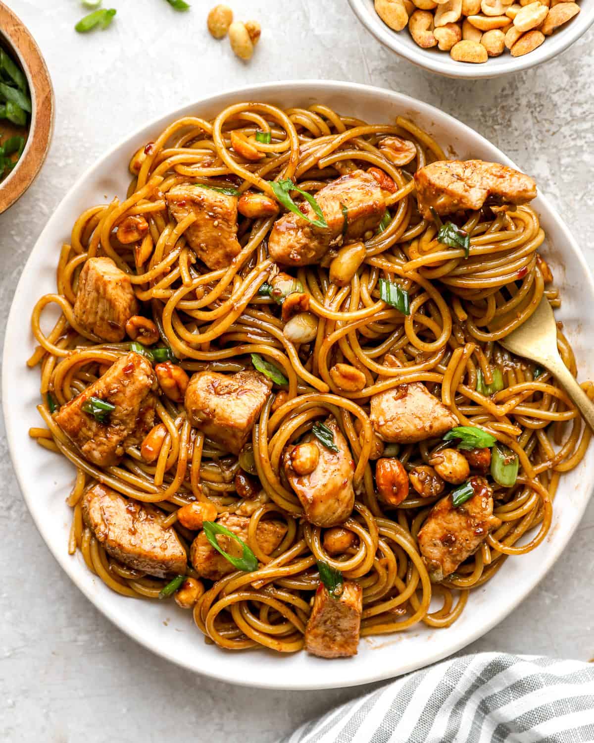 Overhead view of kung pao spaghetti on a white plate, tossed with chicken, peanuts, and green onions