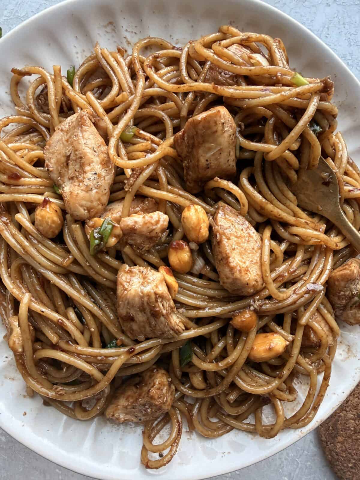 Close-up of a plate of kung pao spaghetti topped with roasted peanuts and green onions