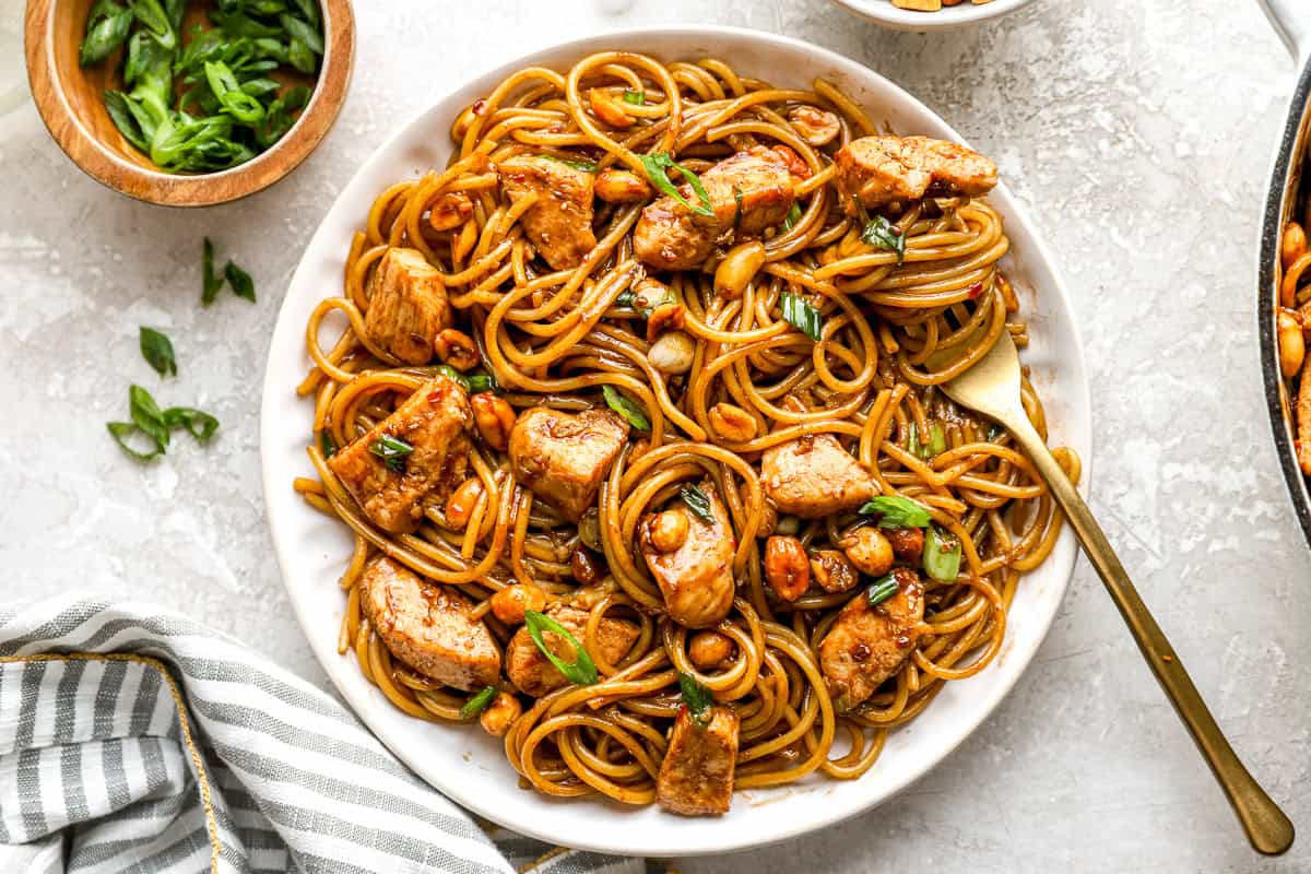 Overhead shot of kung pao spaghetti served on a white plate with a gold fork