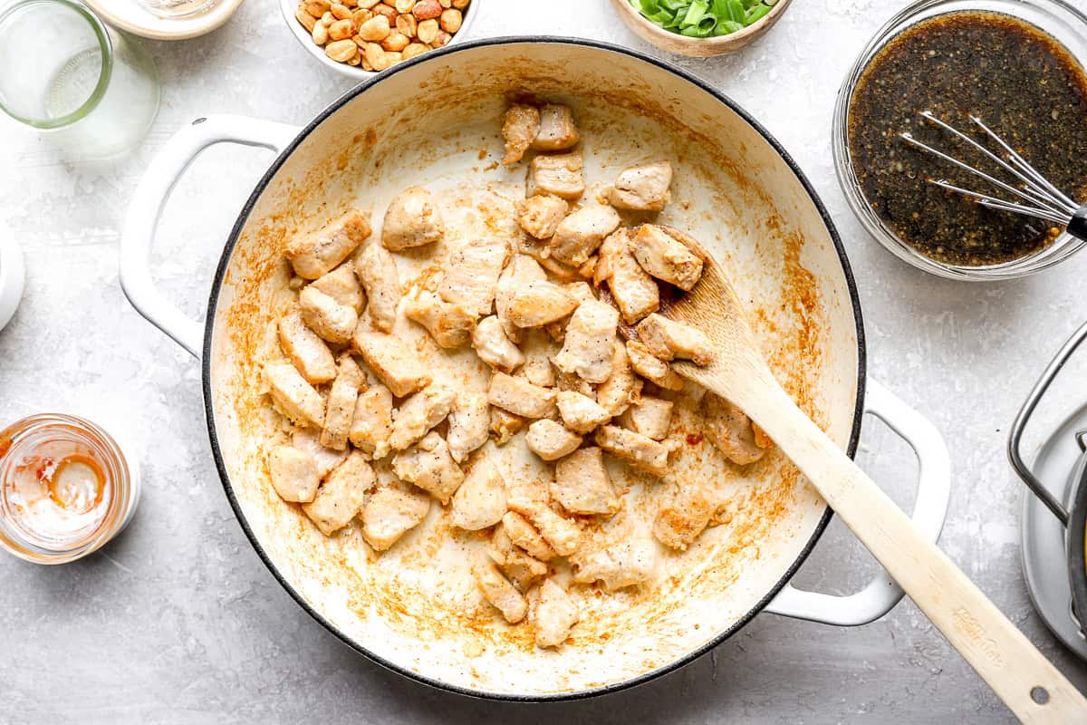 Diced chicken breast cooking in a white skillet for kung pao spaghetti