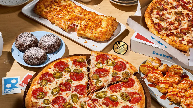 An assortment of Domino's menu items sit on a wooden table, including Pepperoni Pizza,  cheese bread, lava cakes and chicken bites