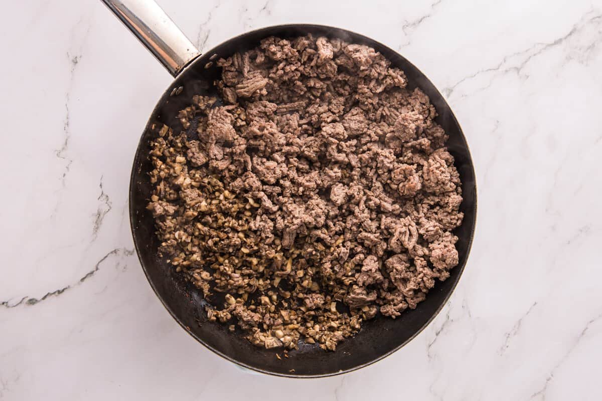 Overhead view of ground beef browned in a skillet next to finely chopped mushrooms before combining