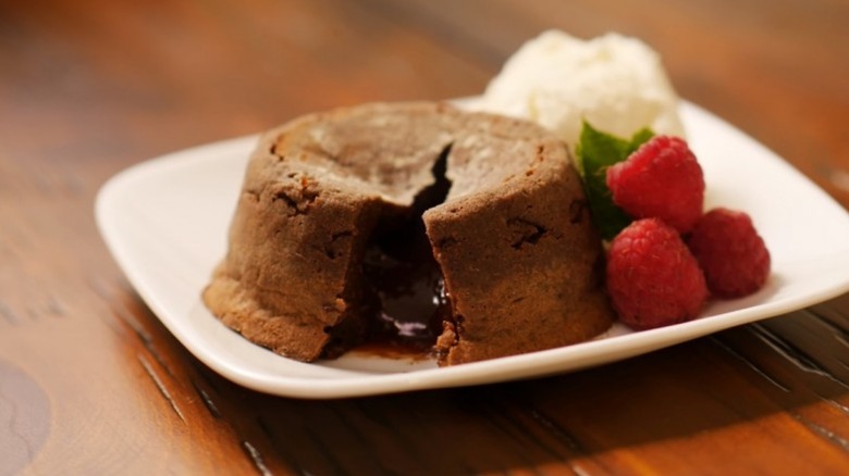 Molten chocolate cake on white plate with raspberries and cream