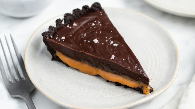 Slice of chocolate caramel tart on white plate