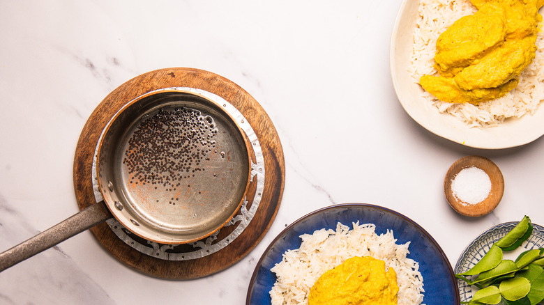 Holding saucepan with tempered oil with mustard seeds.
