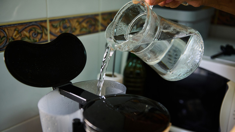 A person filling a coffee maker reservoir with fresh water