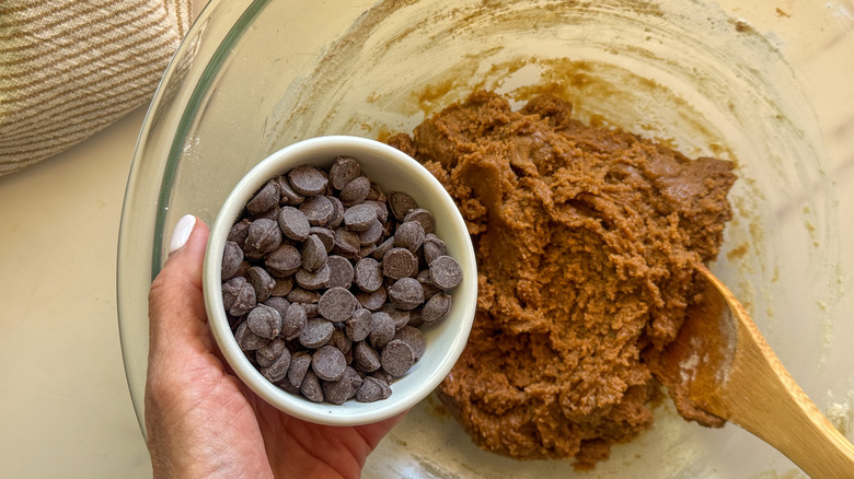 hand adding chocolate chips to cookie dough