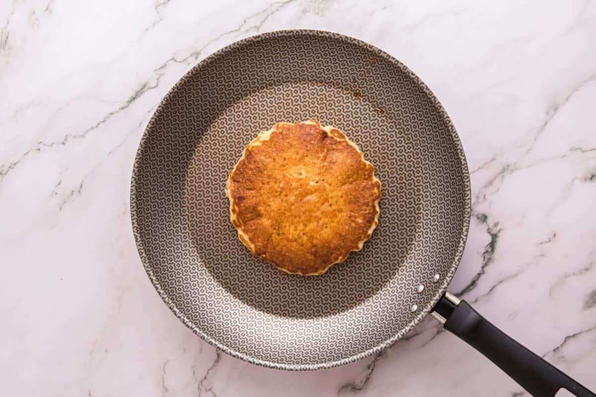 A golden brown pancake cooking in a nonstick skillet
