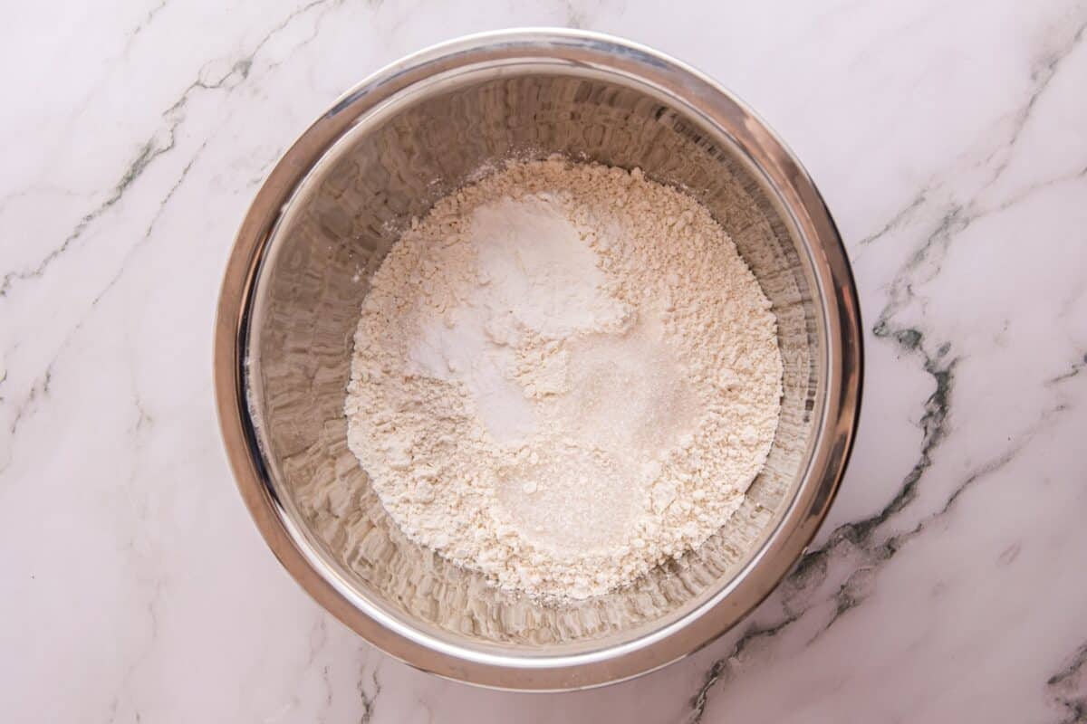 Flour mounded in a stainless steel mixing bowl for the pancake batter