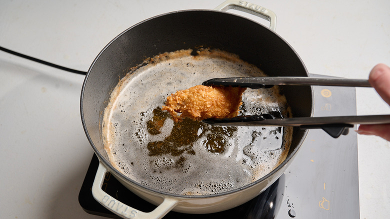 lifting a fried chicken wing out of pot of hot oil