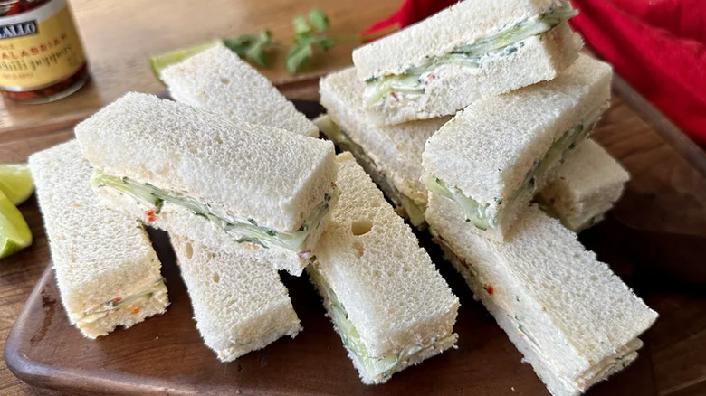 Cucumber finger sandwiches stacked on a cutting board.