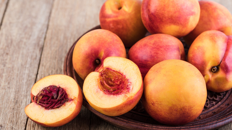 A wooden bowl of nectarines with one sliced fruit